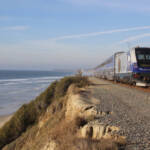 Passenger train on track on hillside above ocean