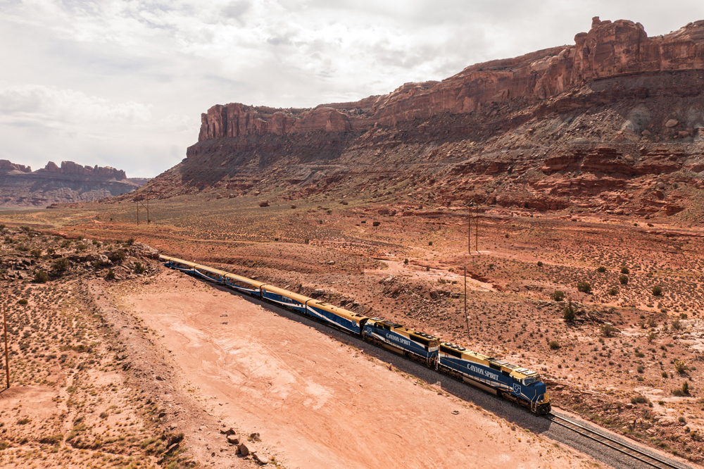 Blue, copper, and white passenger train in canyon with red rocks