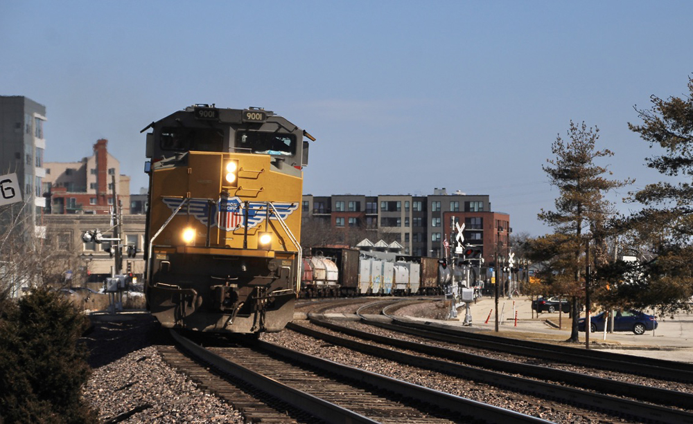 Train with yellow locomotive on curve through surburan community